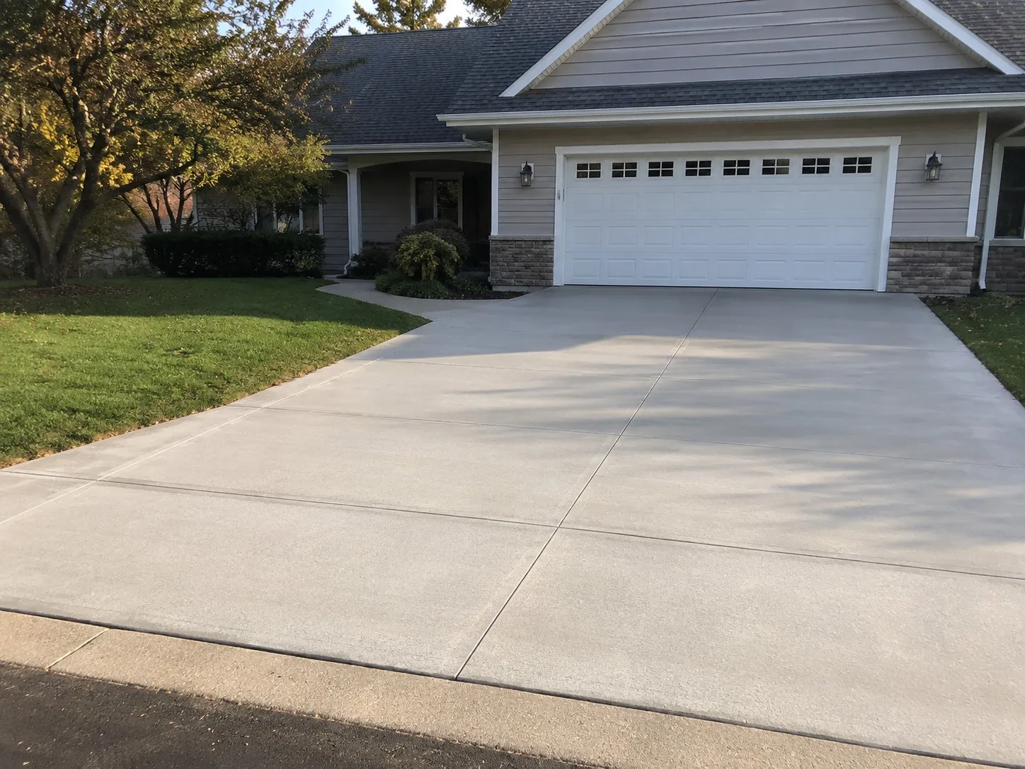 Wide broom-finished concrete driveway with clean control joints running up to a two-car garage