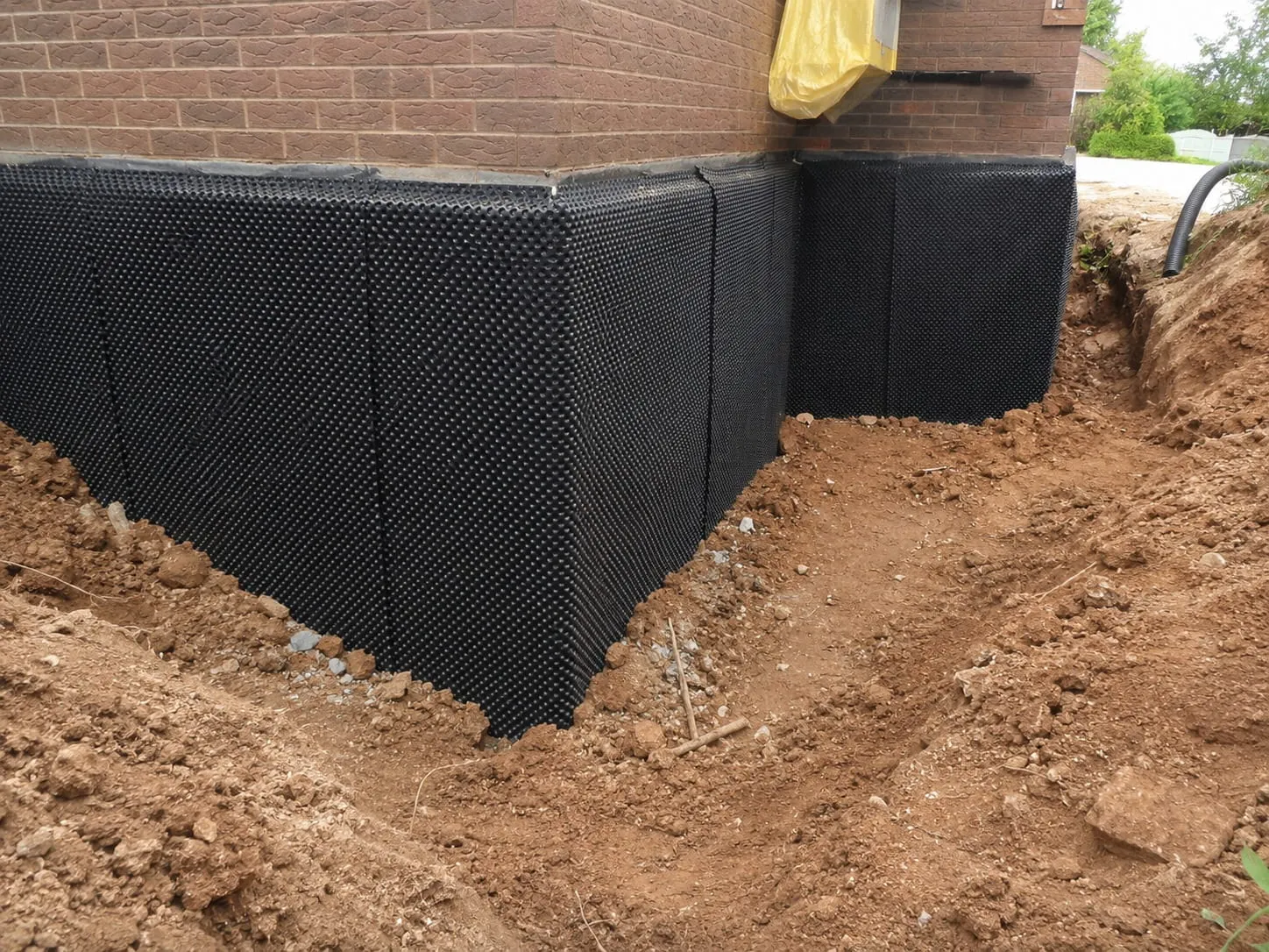 Dimpled damp proofing membrane wrapping the corner of an excavated brick foundation in Washington DC