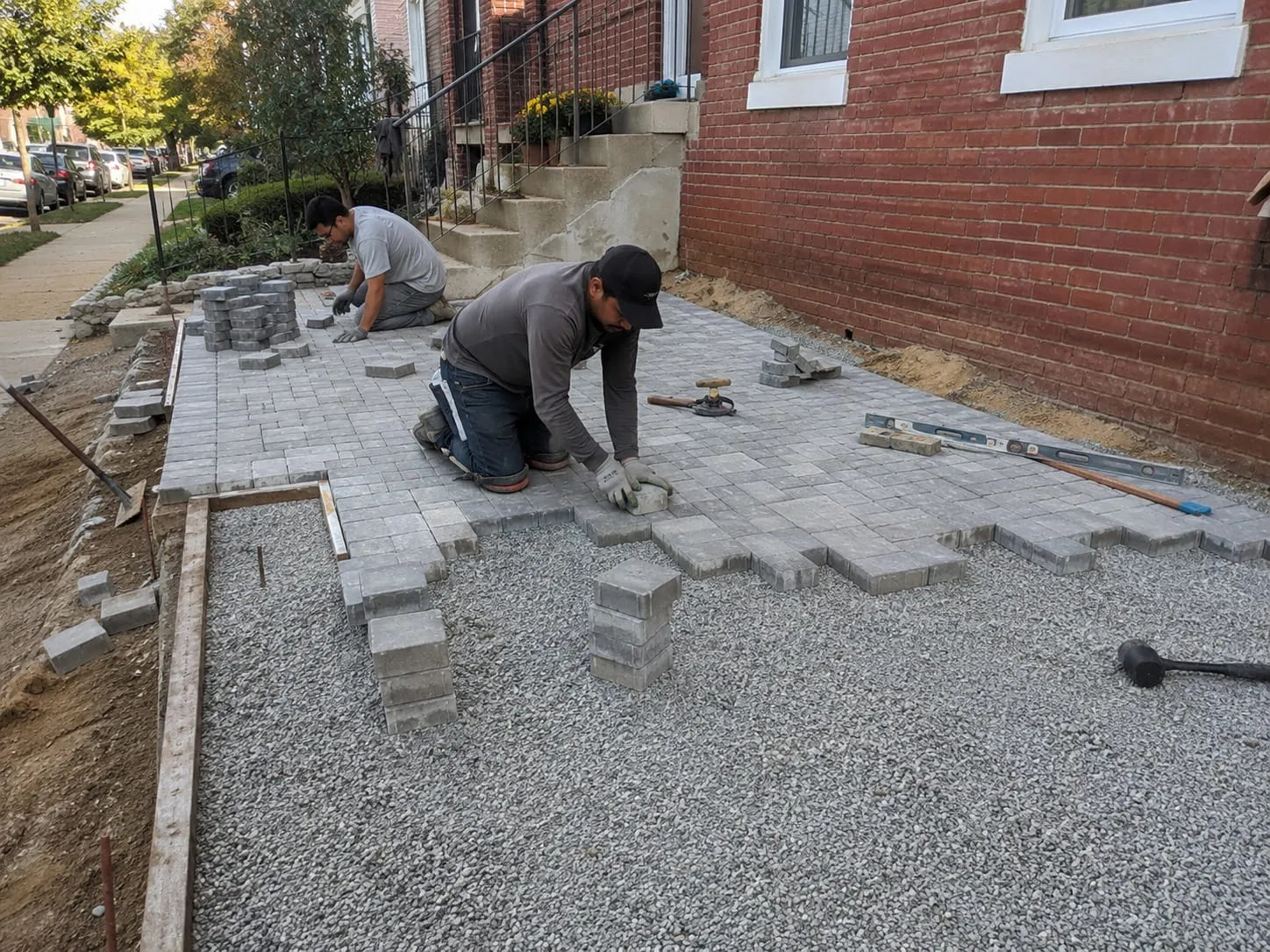 Masons setting pavers against a stone edging border alongside a Washington DC rowhouse