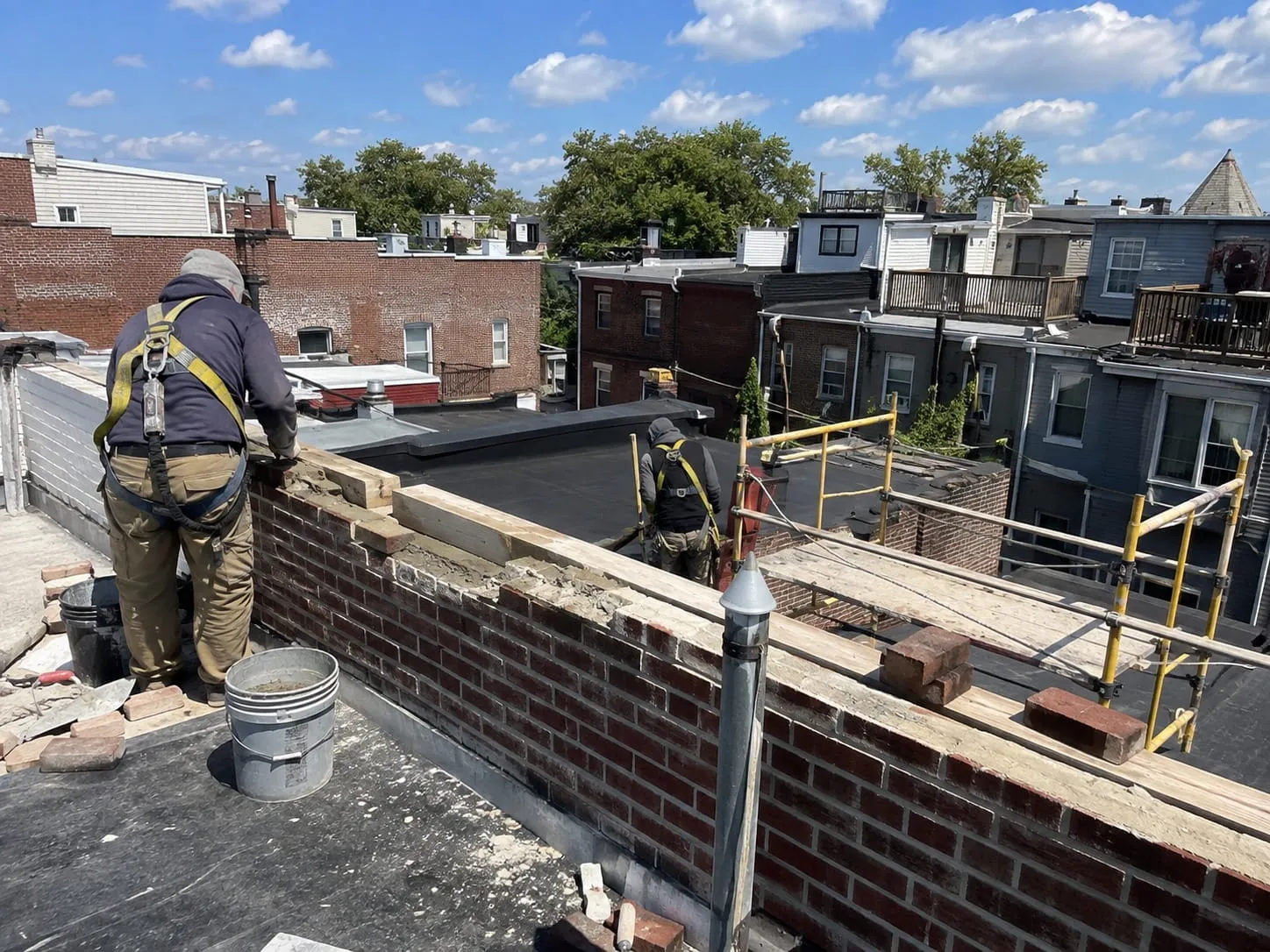 Harnessed masons rebuilding a brick parapet wall on a Washington DC rowhouse rooftop