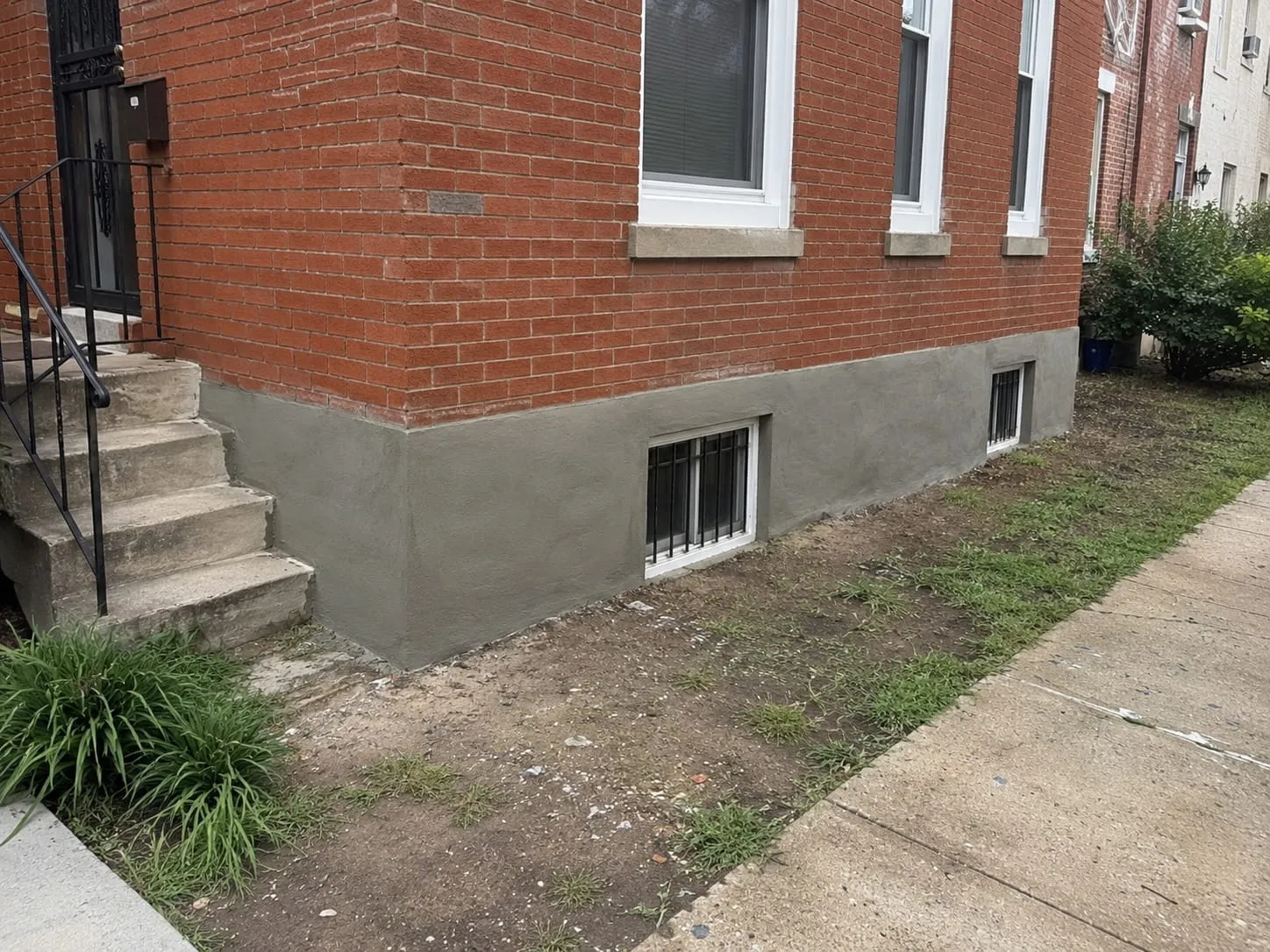 Freshly parged foundation wall wrapping the corner of a red brick rowhouse in Washington DC